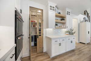 Kitchen featuring white cabinetry, double oven, light wood-style floors, open shelves, and glass insert cabinets