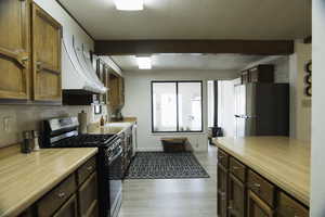 Kitchen with stainless steel appliances, beamed ceiling, light countertops, wood finish cabinets, and light LVP flooring.