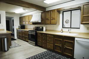 Kitchen featuring stainless steel appliances, light countertops, range hood, LVP floors, and beamed ceiling