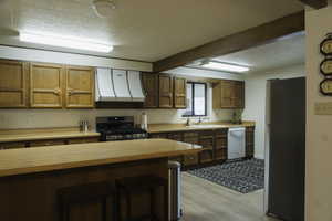 Kitchen with light countertops, stainless steel appliances, wood finish cabinetry, a textured ceiling, and light wood-style flooring