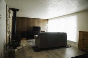 Living area with wooden walls, wood finished floors, a textured ceiling, and a wood stove