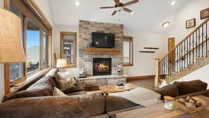 Living room with wood finished floors, stairway, lofted ceiling, a stone fireplace, and ceiling fan