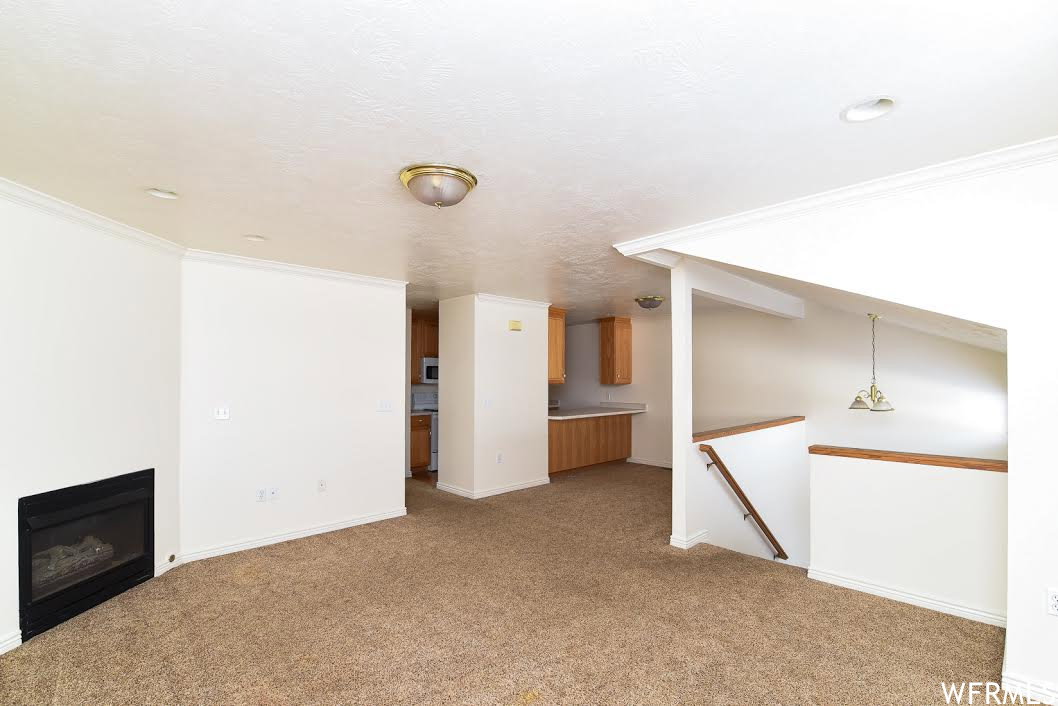 Unfurnished living room featuring crown molding, a glass covered fireplace, and light carpet
