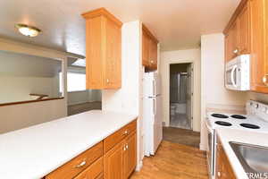 Kitchen with white appliances, light wood-type flooring, light countertops, and wood finish cabinets