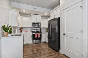 Kitchen with stainless steel appliances, white cabinets, dark wood-style flooring, light stone counters, and backsplash