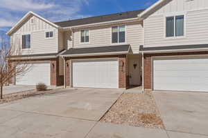 View of front of home featuring board and batten siding, roof with shingles, brick siding, and concrete driveway