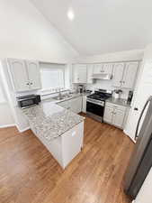Kitchen with a peninsula, stainless steel appliances, vaulted ceiling, light stone countertops, and a kitchen bar