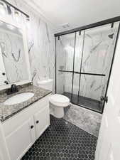 Full bath with vanity, a marble finish shower, tile walls, and crown molding (basement bathroom)
