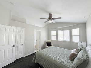 Master bedroom featuring lofted ceiling, dark colored carpet, ensuite bath, and a ceiling fan