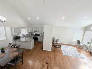 Kitchen featuring lofted ceiling, stainless steel appliances, light stone counters, gray cabinetry, and dark wood-style flooring