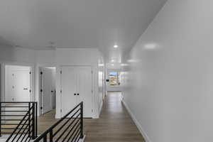 Hallway with wood finished floors, recessed lighting, and an upstairs landing