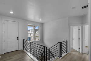 Hallway with an upstairs landing, wood finished floors, and recessed lighting