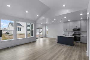 Kitchen with open floor plan, a kitchen island with sink, stainless steel appliances, french doors, and light wood-style floors