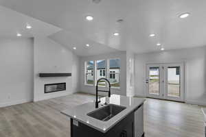Kitchen featuring a center island with sink, open floor plan, a glass covered fireplace, light stone countertops, and healthy amount of natural light