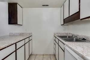 Kitchen featuring white dishwasher, light countertops, light tile patterned floors, and two tone color scheme