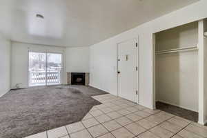 Unfurnished living room featuring light colored carpet, a fireplace, and light tile patterned floors