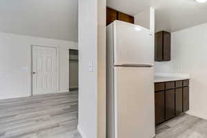 Kitchen with freestanding refrigerator, dark wood finish cabinets, light wood-type flooring, and light countertops