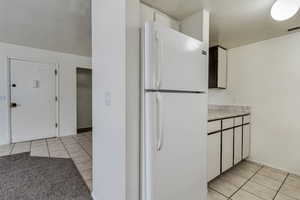 Kitchen featuring freestanding refrigerator, light tile patterned floors, light countertops, and white cabinetry