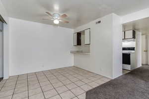 Unfurnished room featuring light tile patterned floors, light carpet, and ceiling fan