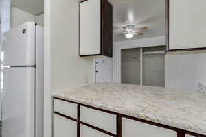 Kitchen with freestanding refrigerator, light countertops, white cabinetry, and a ceiling fan
