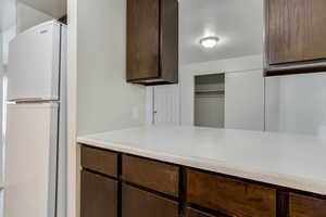 Kitchen featuring freestanding refrigerator, dark wood finish cabinets, and light countertops