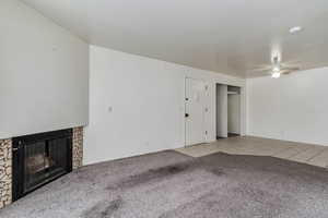Unfurnished living room with a fireplace, light colored carpet, a ceiling fan, and light tile patterned floors