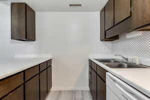 Kitchen with dark wood finish cabinets, dishwasher, decorative backsplash, and light countertops