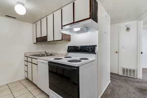 Kitchen with electric stove, light countertops, white dishwasher, light tile patterned floors, and two tone cabinets