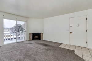 Unfurnished living room with light colored carpet, a fireplace, and light tile patterned floors