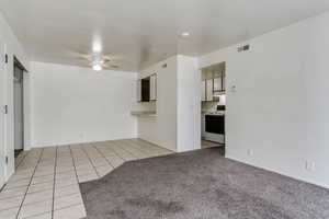 Unfurnished living room featuring light tile patterned flooring, ceiling fan, and light colored carpet