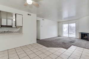 Unfurnished living room with a ceiling fan, light colored carpet, a fireplace, and light tile patterned floors