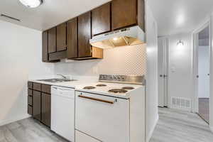 Kitchen featuring white appliances, light countertops, dark wood finish cabinets, light wood-type flooring, and tasteful backsplash