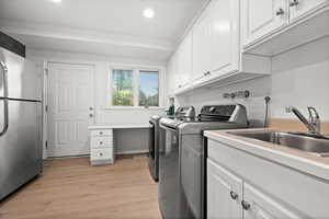 Laundry room with light wood-style flooring, washer and clothes dryer, and crown molding
