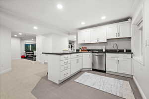 Kitchen featuring dark countertops, white cabinetry, a peninsula, dishwasher, and crown molding