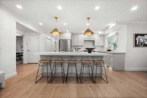 Kitchen with ornamental molding, a breakfast bar area, hanging light fixtures, a center island with sink, and high quality fridge