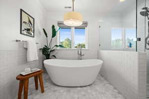 Bathroom with tile walls, a stall shower, a wainscoted wall, crown molding, and a soaking tub