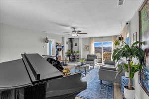 Living area with a wood stove, ceiling fan, wood finished floors, a mountain view, and a textured ceiling