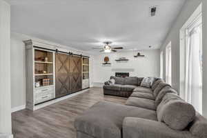 Living area featuring a barn door, wood finished floors, ceiling fan, a brick fireplace, and brick wall