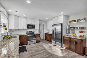 Two tone kitchen featuring two tone cabinets, open shelves, light stone counters, stainless steel appliances, and light wood-type flooring