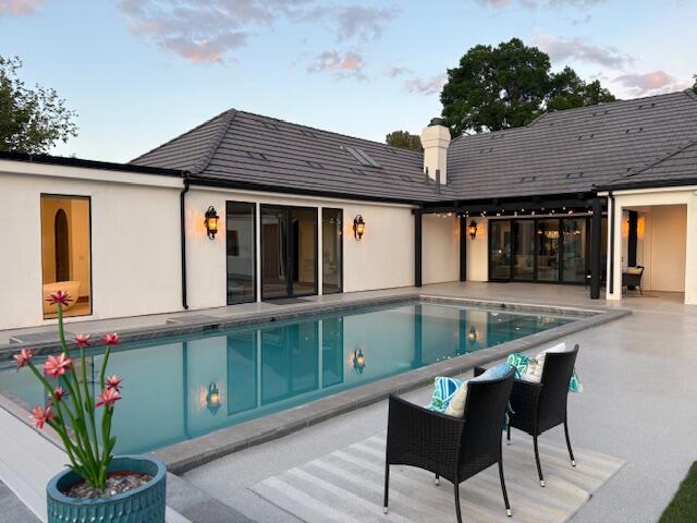 Rear view of property with a patio area, an outdoor pool, a chimney, and stucco siding