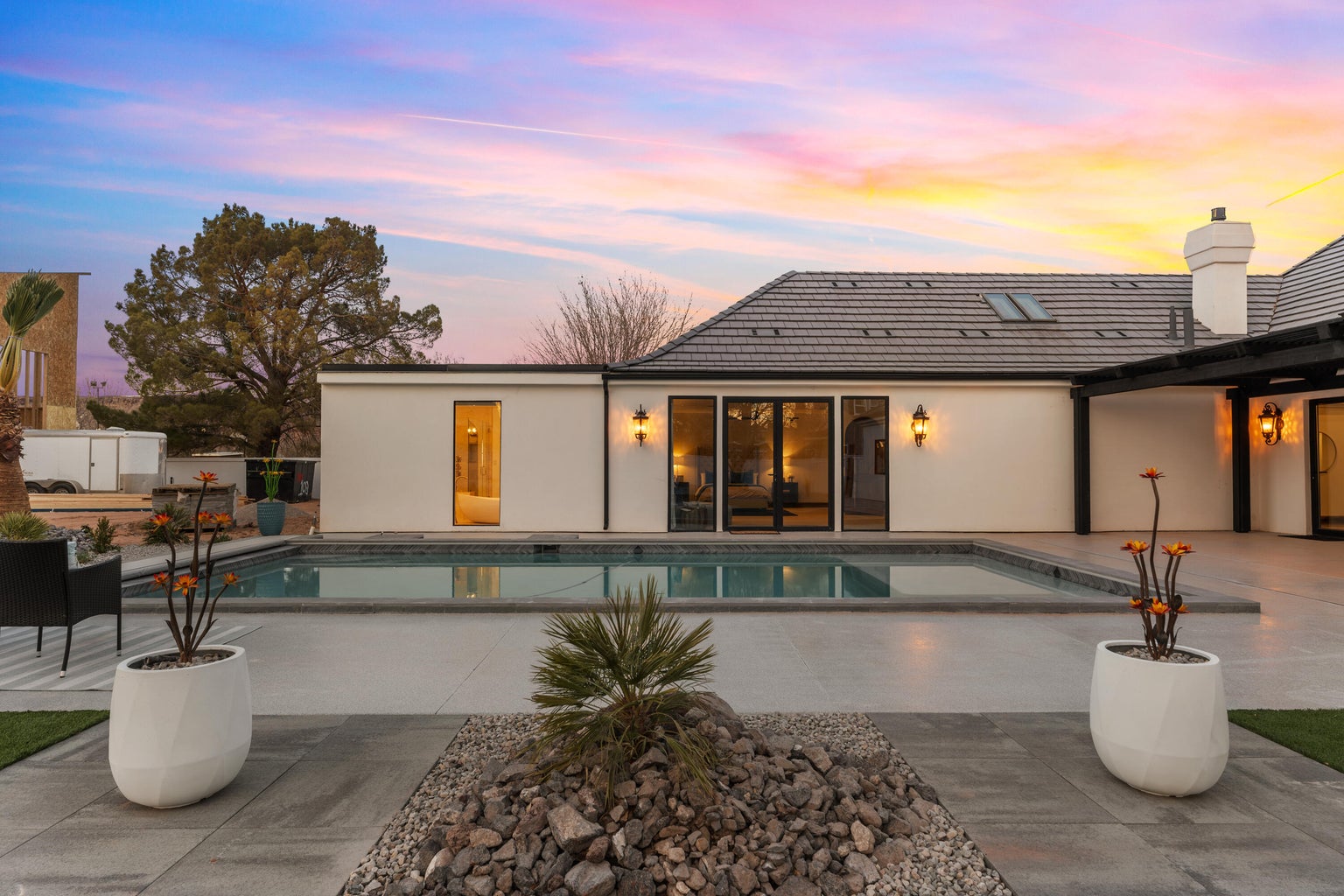 Back of property at dusk featuring a patio, an outdoor pool, a chimney, stucco siding, and a tiled roof