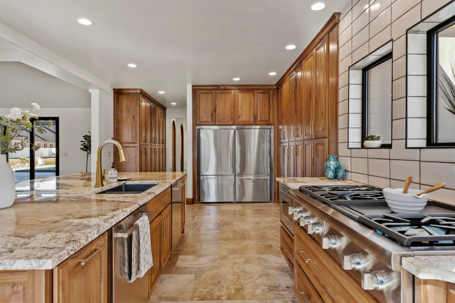 Kitchen featuring wood finish cabinets, stainless steel appliances, recessed lighting, light stone counters, and a center island with sink
