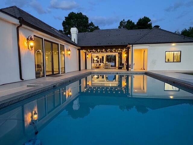 Back of house at dusk featuring a patio area, a chimney, and an outdoor pool