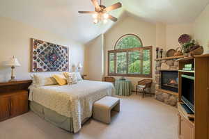 Bedroom featuring carpet flooring, ceiling fan, and a stone fireplace