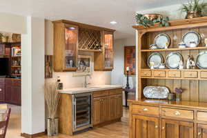Indoor wet bar featuring beverage cooler, wood finish cabinetry, light countertops, light wood finished floors, and glass insert cabinets