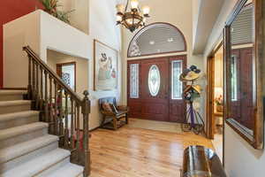 Entryway with light wood finished floors, a chandelier, and a high ceiling