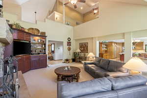 Living room featuring light colored carpet, a ceiling fan, a chandelier, and a high ceiling