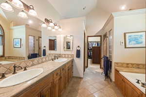 Full bathroom featuring a garden tub, decorative backsplash, double vanity, stone tile floors, and ornamental molding