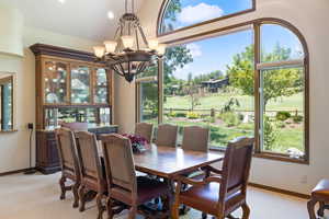 Dining room featuring light carpet, golf course view, lofted ceiling, and a chandelier