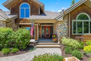 Property entrance featuring a porch, stone siding, and roof with shingles